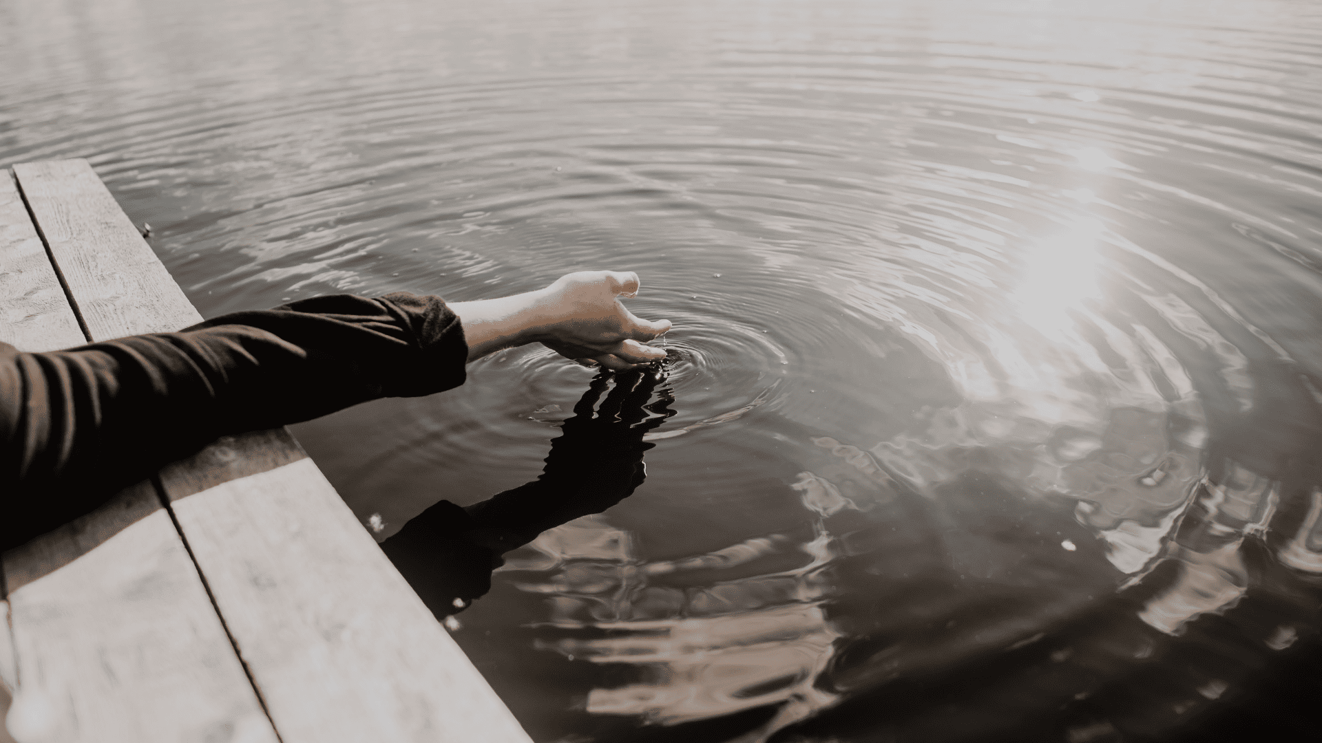 Ein Arm, der mit der Hand von einem Steg aus ins Wasser greift