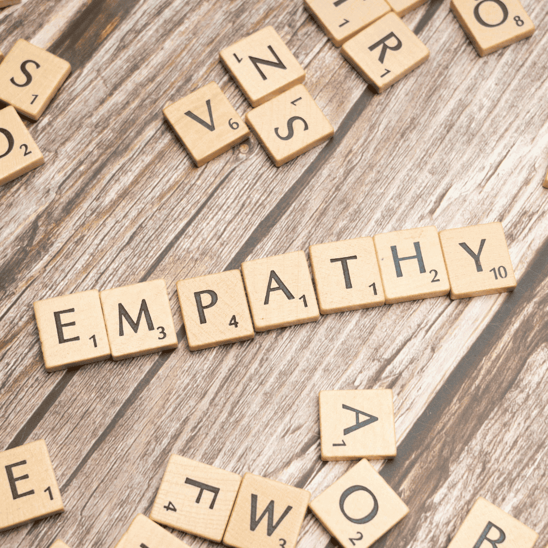 Verschiedene Holzsteine, auf denen Buchstaben zu sehen sind. In der Mitte dieser Steine ist das Wort empathy ersichtlich.