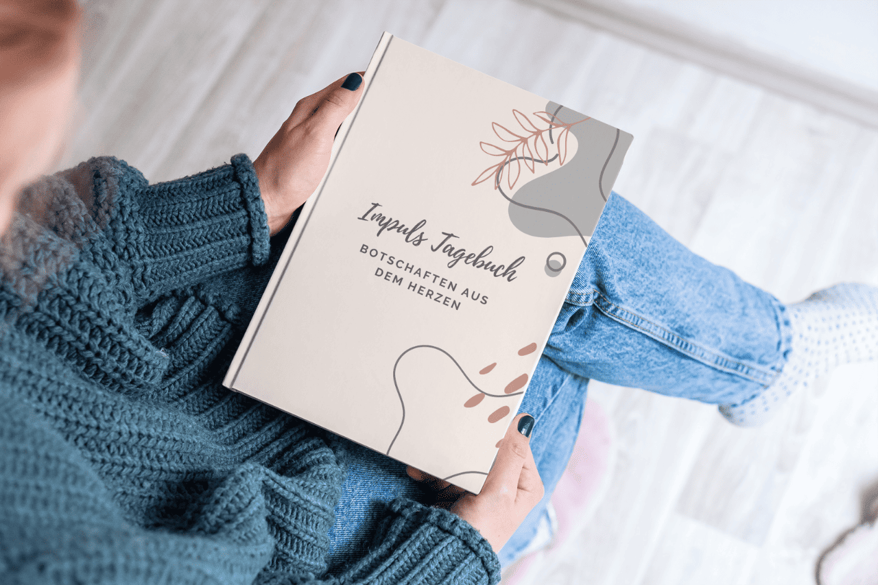 Intuition Impuls Tagebuch Eine Frau im grünen Pullover, einer blauen Jeans und weißen Turnschuhen sitzt und hält mein Buch "Impuls Tagebuch - Botschaften aus dem Herzen" in ihren Händen.