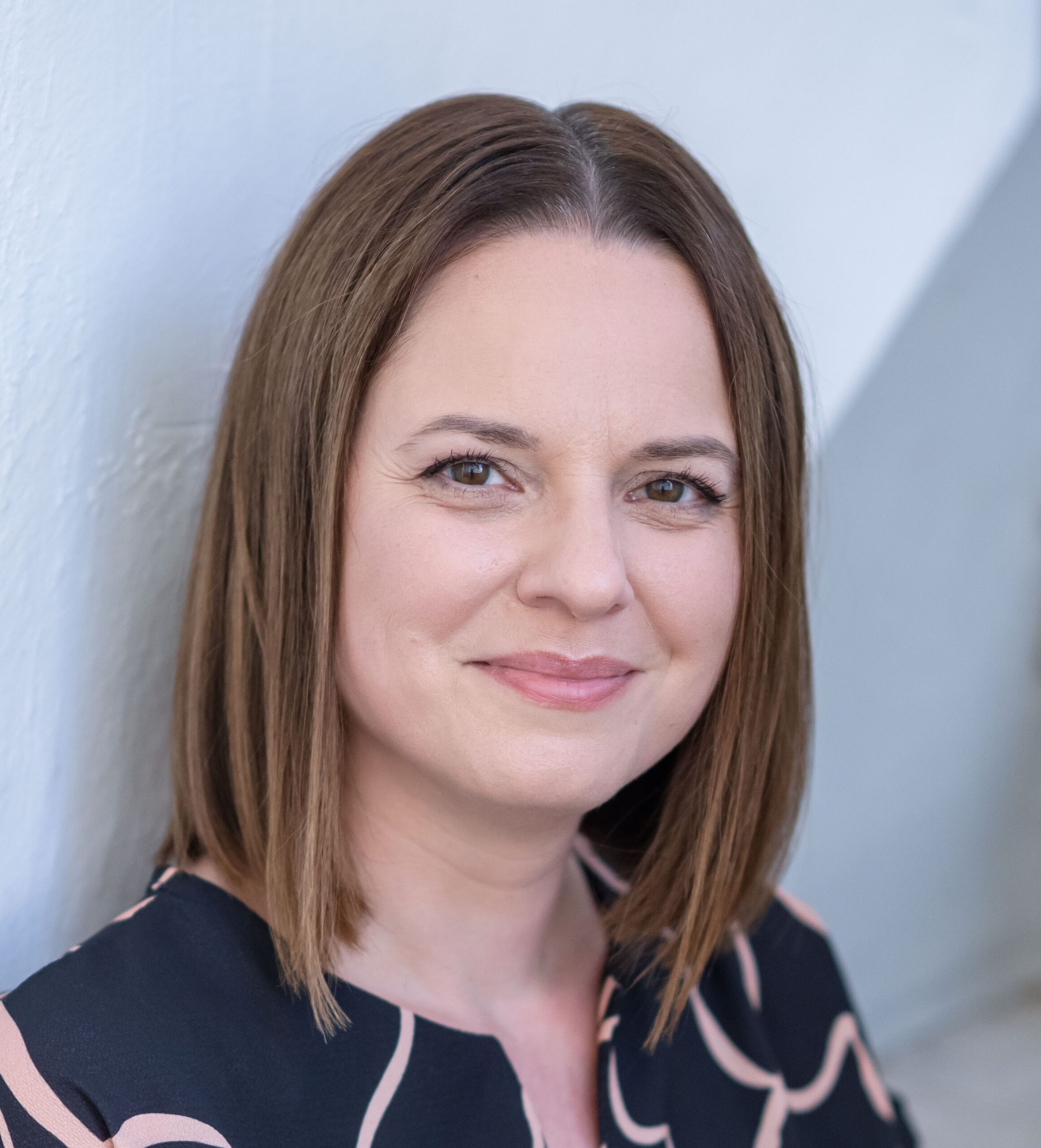 Mehr Geld am Ende des Monats: Eine Frau mit kurzen dunklen Haaren und einem schwarzen Kleid mit orangen Mustern, die auf einer Stiege angelehnt an einer Wand sitzt.