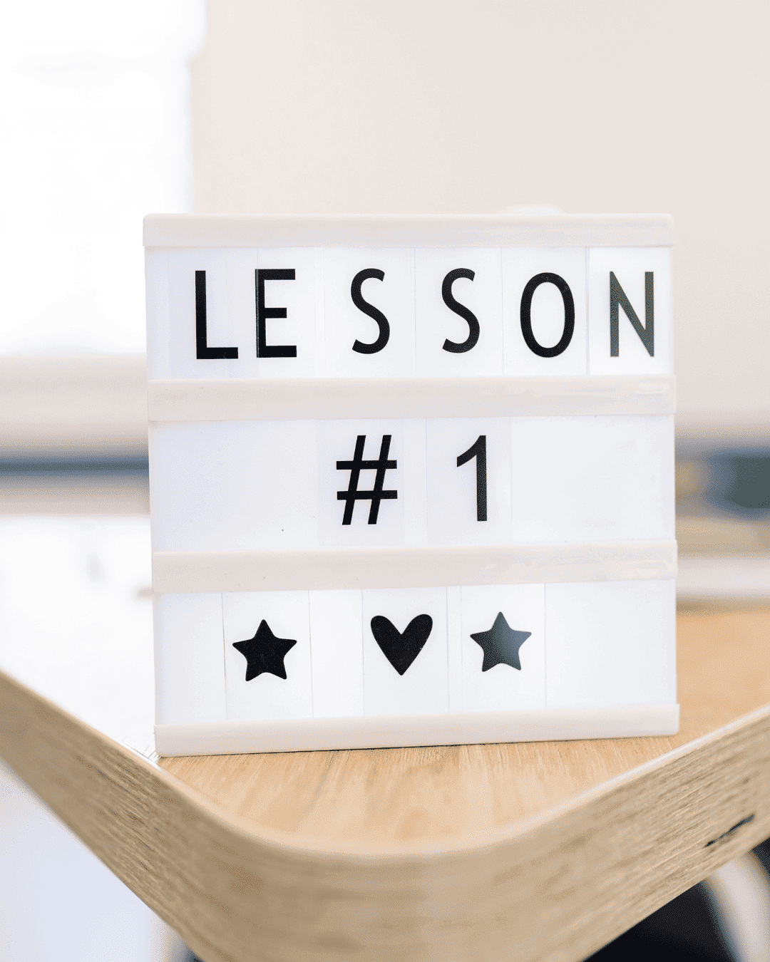 Nachhilfe in Oberösterreich: Auf dem Bild ist die Kante eines beigen Tisches, auf dem ein Schild mit Lesson #1 mit Sterne und Herz steht.